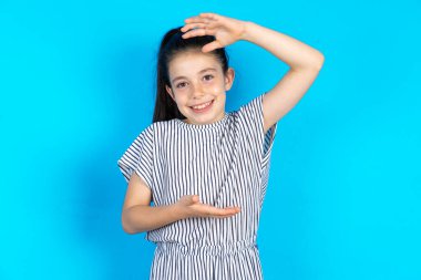 Mavi arka planda çizgili elbise giyen güzel bir kız. Elleri büyük ve büyük boy işareti, ölçü sembolü gösteriyor. Kameraya bakıp gülümsüyor..