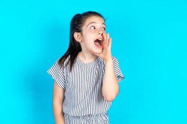 Beautiful kid girl wearing striped dress over blue background hear incredible private news impressed scream share clipart