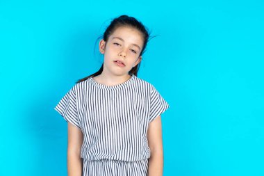 Sıkılmış, güzel bir kız çocuğu mavi arka planda çizgili bir elbise giyer, el ele tutuşur, diğer yandan da yorgun ve hasta görünür, uykulu ve yorgun görünür, yorgunluk ve akşamdan kalmalıktan bitap düşer, sabahları tembel gözler..