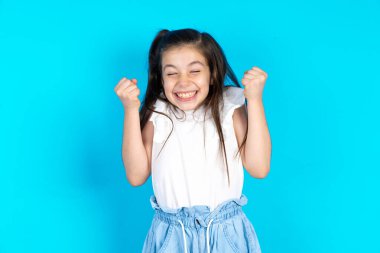 Mavi stüdyonun arkasında duran güzel beyaz kız kollarını kaldırarak ve gözleri kapalı zaferi kutlayarak başarı için heyecanlanıyor. Kazanan konsept.