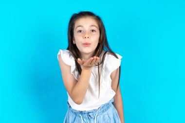 Kameraya bakan bir çocuk havayla öpüşürken güzel ve seksi görünüyor. Aşk ifadesi. Güzel beyaz kız mavi stüdyo arka planında poz veriyor.