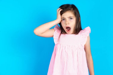 Şok olmuş yüzü olan utangaç bir çocuk, şaşkınlığını ifade ediyor, şaşırmış bir model içeride poz veriyor. Güzel beyaz kız mavi stüdyo arka planında poz veriyor.