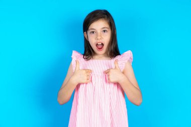 Utangaç bir kız, şaşkın bir ifadeyle yarışmaya katıldığı için şoka uğruyor, bir konuda tereddüt ediyor. Güzel beyaz kız mavi stüdyo arka planında poz veriyor.