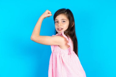 Güçlü, neşeli bir çocuğun kaslarını gösteren portresi. Güzel beyaz kız mavi stüdyo arka planında poz veriyor.