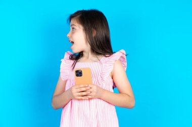 Akıllı telefonu olan bir çocuk boş bir boşluğa yan bakıyor. Güzel beyaz kız mavi stüdyo arka planında poz veriyor.