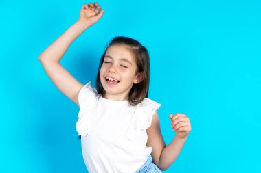 Neşeli çocuk fotoğrafı. Eğleniyor ve kaygısız dans ediyor. Güzel beyaz kız mavi stüdyo arka planında poz veriyor.