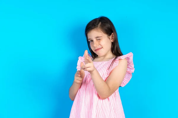 Радостная Красивая Маленькая Девочка Розовом Платье Голубом Фоне Подмигивает Указывает — стоковое фото