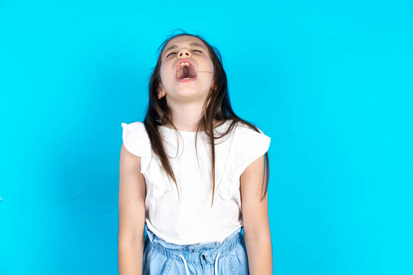 Beautiful caucasian kid girl standing over blue studio background angry and mad screaming frustrated and furious, shouting with anger. Rage and aggressive concept.