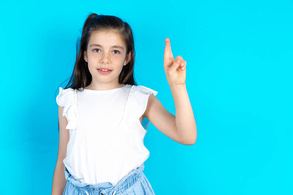 kid pointing up with fingers number ten in Chinese sign language. Beautiful caucasian little girl posing over blue studio background