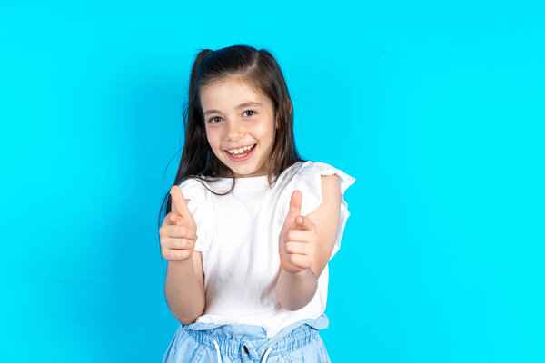 kid directs fingers at camera, selects someone. I recommend you. Best choice. Beautiful caucasian little girl posing over blue studio background