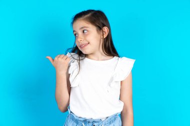 Çocuk işaret ediyor ve reklam yapıyor. Güzel beyaz kız mavi stüdyo arka planında poz veriyor.