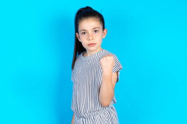 Çocuk yumruğunu gösterdi. Yüzünde sinir bozucu bir ifade var. İntikam almak ya da birini tehdit etmek ciddi bir bakış getiriyor. Sana patronun kim olduğunu göstereceğim. Mavi stüdyo arka planında duran güzel beyaz kız 