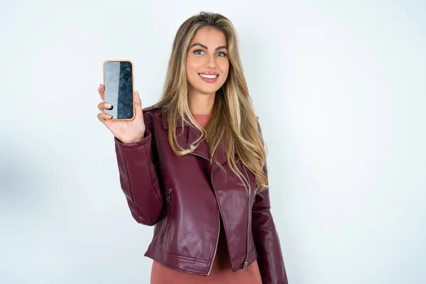 Usmívající Mladá Běloška Kožené Bundě Drží Mobilní Telefon Prázdnou Obrazovkou — Stock fotografie