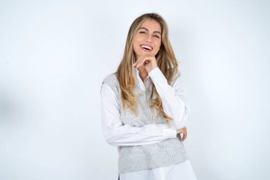 İyimser, beyaz gömlek giyen beyaz kadın ellerini çapraz yapıyor ve elleri çenenin altında, kameraya zevkle bakıyor..