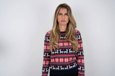 Tatmin olmamış Kafkasyalı bir kadının Noel süveteri giymesi ve kamerada hayal kırıklığına uğrayan bir şey yüzünden keyifsiz bir yüz ifadesi.