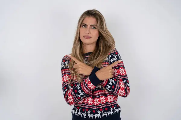 クリスマスセーターを着用した真剣な白人女性は 2つのアイテムの間で躊躇するさまざまな側面で手とポイントを交差します ハード決定コンセプト — ストック写真