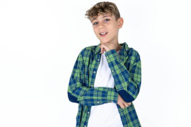 Beyaz stüdyo arka planındaki iyimser yakışıklı beyaz çocuk elleri çapraz ve elleri çenenin altında, zevkle kameraya bakıyor..