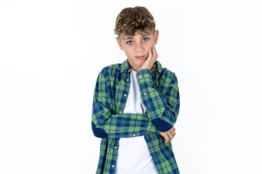 Sıkılmış, yakışıklı, beyaz tenli beyaz bir çocuk stüdyo arka planında el ele tutuşurken diğer eli çapraz yapmış, yorgun ve hasta görünüyor.,