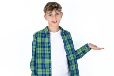 Beyaz stüdyo arka planındaki yakışıklı beyaz çocuk mutlu bir şekilde sunum yapıyor ve avuç içi kameraya bakıyor..