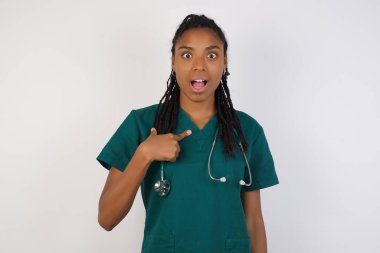 Şaşırmış güzel doktor kadın sersemlemiş durumda, şaşkın bir şekilde kendini parmağıyla işaret ederek 