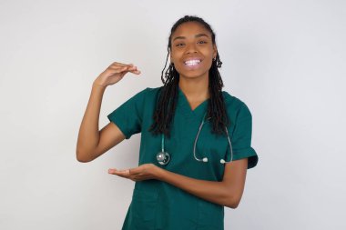 Afrikalı Amerikalı doktor kadın izole edilmiş arka plan hareketleriyle büyük ve büyük boyut işareti, ölçü sembolü gösteriyor. Kameraya bakıp gülümsüyor. Ölçüm konsepti.