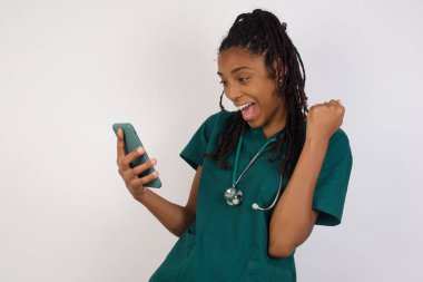 Mutlu, Afro-Amerikan doktor bir kadının portresi başarıyı kutlarken ayakta duruyor ve cep telefonuna bakıyor..