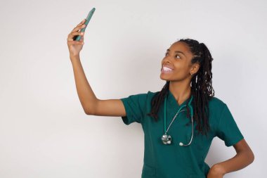 Oldukça mutlu bir Afro-Amerikan doktor kadının portresi. Parlak arka planda izole edilmiş bir selfie çekiyor.