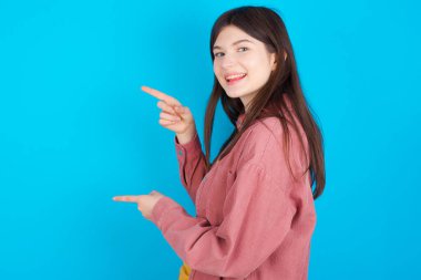 Mavi arka plan noktalarından izole edilmiş pembe tişört giyen genç beyaz kız ağzı açık şaşırmış yüz ifadesi ile şaşırtıcı bir şey gösteriyor. Reklam kavramı.