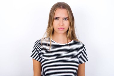 Beyaz arka planda çizgili tişört giyen güzel sarışın kız ciddi bir yüze sahip. 