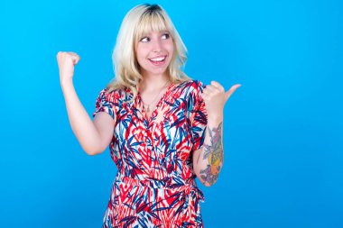 Yaşasın beyaz kız, çiçekli elbise giyiyor. Mavi arka planda izole edilmiş. Boş uzay eli yumruğu.