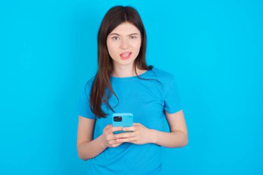 Mavi tişört giyen çılgın, beyaz bir kızın mavi arka planda izole edilmiş fotoğrafı geri bildirim konseptinden uzak dur.