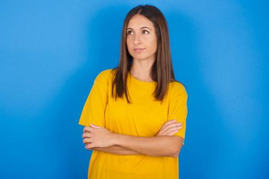 Düşünceli, düşünceli, genç bir kadın kollarını kavuşturmuş, düşünceli bir ifadeyle ne yapacağını düşünüyor.