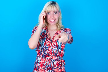 Mavi arka planda izole edilmiş çiçek desenli elbise giyen beyaz bir kız doğrudan kameraya bakarak uzun saatlerce konuşmaktan keyif aldığını gösteriyor. Bana katıl.