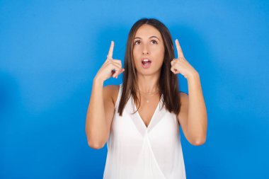 Güzel genç bir kadın şaşırmış ve şaşırmış görünüyor ve parmaklarıyla garip bir şey gösteriyor..