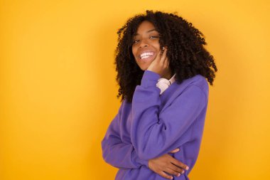 Sarı arka planda kulaklıkları olan Afro-Amerikan bir kadının portresi.