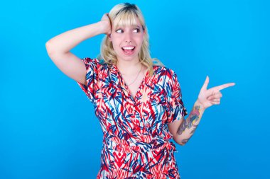 Mavi arka planda izole edilmiş çiçek desenli elbise giyen beyaz bir kız el ele tutuşarak boş alanı işaret ediyor.