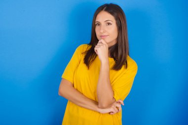 Güzel, genç bir kadın. Çenesinin altında ve yana bakıyor. Şüpheli ve şüpheci bir ifade takınıyor..