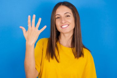 Güzel genç bir bayan gülümsüyor ve arkadaş canlısı görünüyor, 5 ya da 5 numarayı gösteriyor, elleri önde, geri sayıyor.