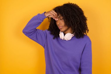 Sarı arka planda kulaklıkları olan depresif Afrikalı Amerikalı bir kadının portresi.