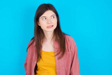 Tüh! Mavi arka planda izole edilmiş pembe tişört giyen beyaz kızın portresi dişlerini sıkar ve şaşırtıcı bir şekilde kafasını karıştırır. Hatasının farkına varır.,