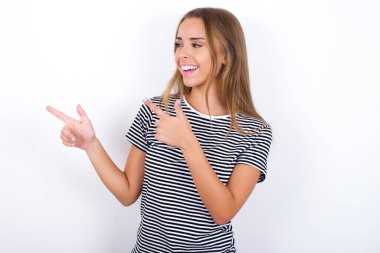 İyimser sarışın kız beyaz arka plan noktalarında çizgili tişört giyiyor ve boş alana bakıyor..