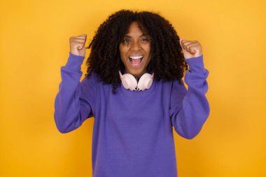 Sarı arka planda kulaklıkları olan Afro-Amerikan bir kadının portresi.