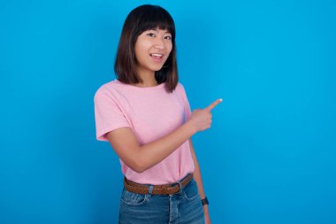 Asyalı genç bir kadın mavi arka planda tişört giyiyor ve sana gülümsüyor. Şuraya bak.!