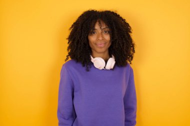 Sarı arka planda kulaklıkları olan Afro-Amerikan bir kadının portresi.