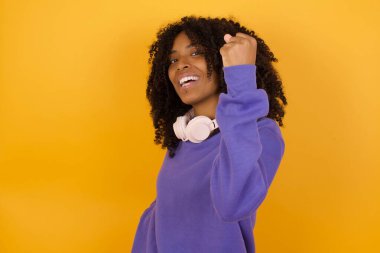 Sarı arka planda kulaklıklı Afro-Amerikalı genç bir kadının portresi zaferi kutluyor.
