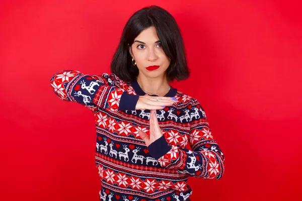 赤い背景にクリスマスのセーターを身に着けているブルネットの慎重な女性はタイムアウトのジェスチャーを示す動揺している 必要性停止 懸命な仕事の後の休息のための時間を頼みます 示します壊れた手の印を壊します — ストック写真