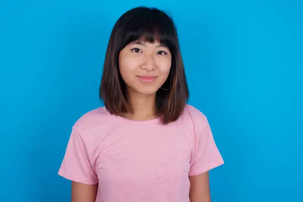 快乐的年轻亚洲女人 穿着蓝色背景的T恤 带着迷人可爱的微笑看着相机 — 图库照片