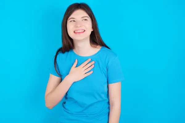 穿着蓝色背景的蓝色T恤的快乐年轻的高加索女孩表现出积极向上的情绪 让人想起一些有趣的事情 让人愉快地手牵着手笑 — 图库照片