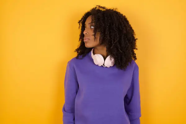 黄色の背景にヘッドフォンを持つ若い表現力のあるアフリカ系アメリカ人女性の肖像画 — ストック写真