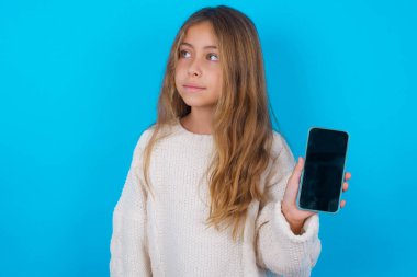 Güzel genç kız yeni cep telefonunu tutuyor ve gizemli görünüyor. Modern cep telefonunun boş görüntülerini gösteriyor.